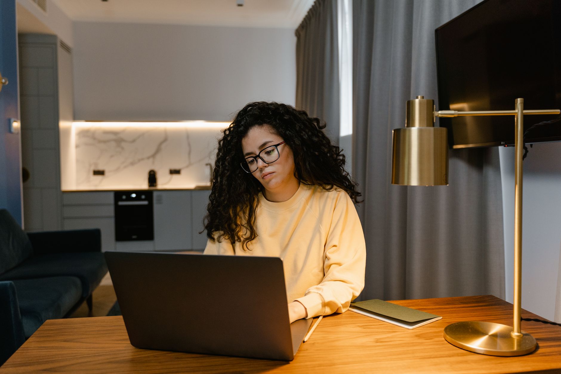 Vrouw in gele trui werkt op een laptop thuis in een gezellig, modern interieur.