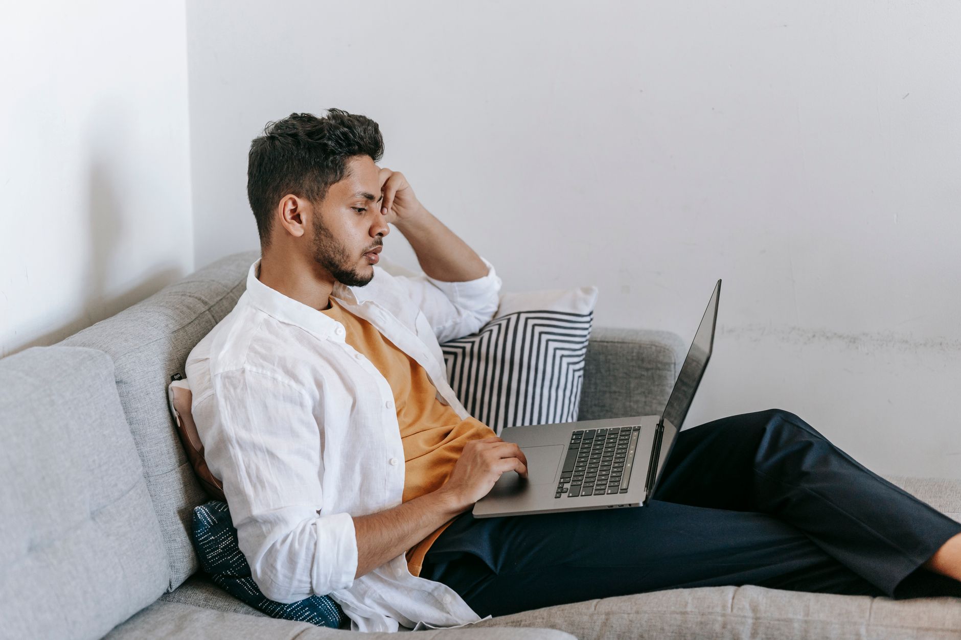 Zijaanzicht van een geconcentreerde jonge man die op de bank een laptop gebruikt voor werk op afstand.